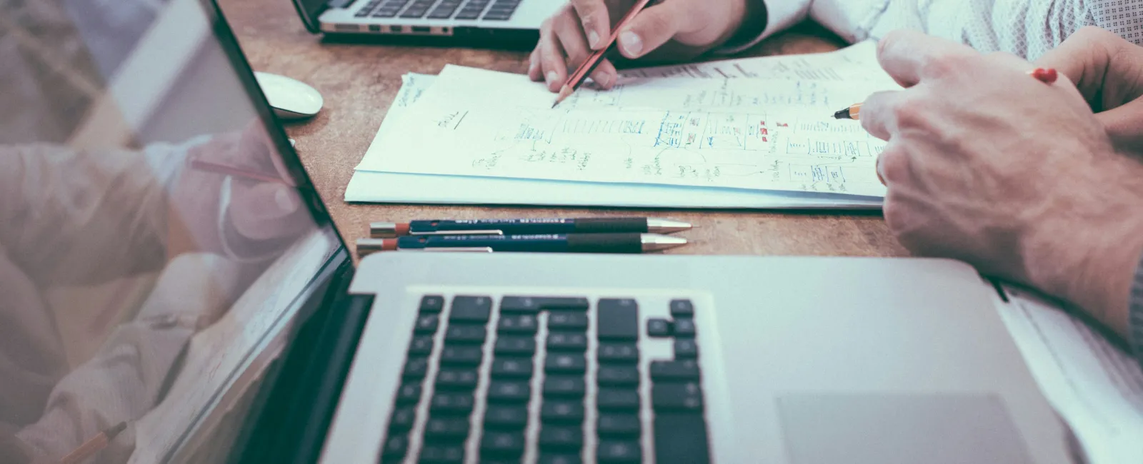 Two professionals collaborate over documents and laptops, planning and analyzing data at a wooden desk.