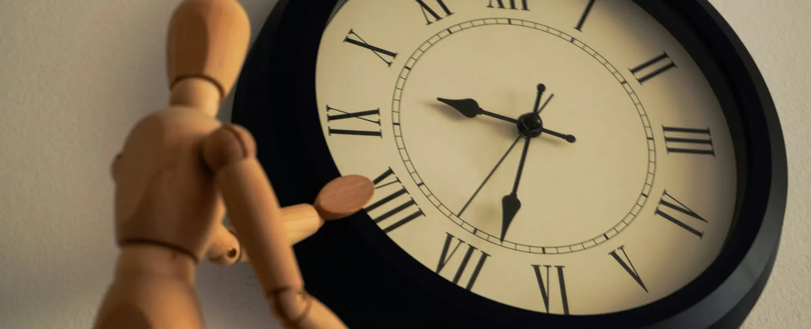 Wooden mannequin pointing at a wall clock showing 5:44 with Roman numerals in warm light.