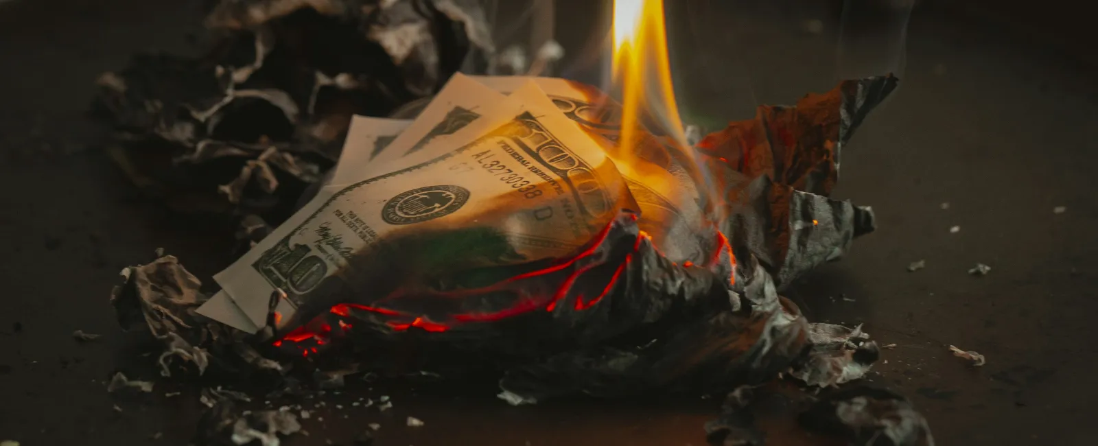 Burning ten-dollar bills with flames consuming the edges on a dark surface.