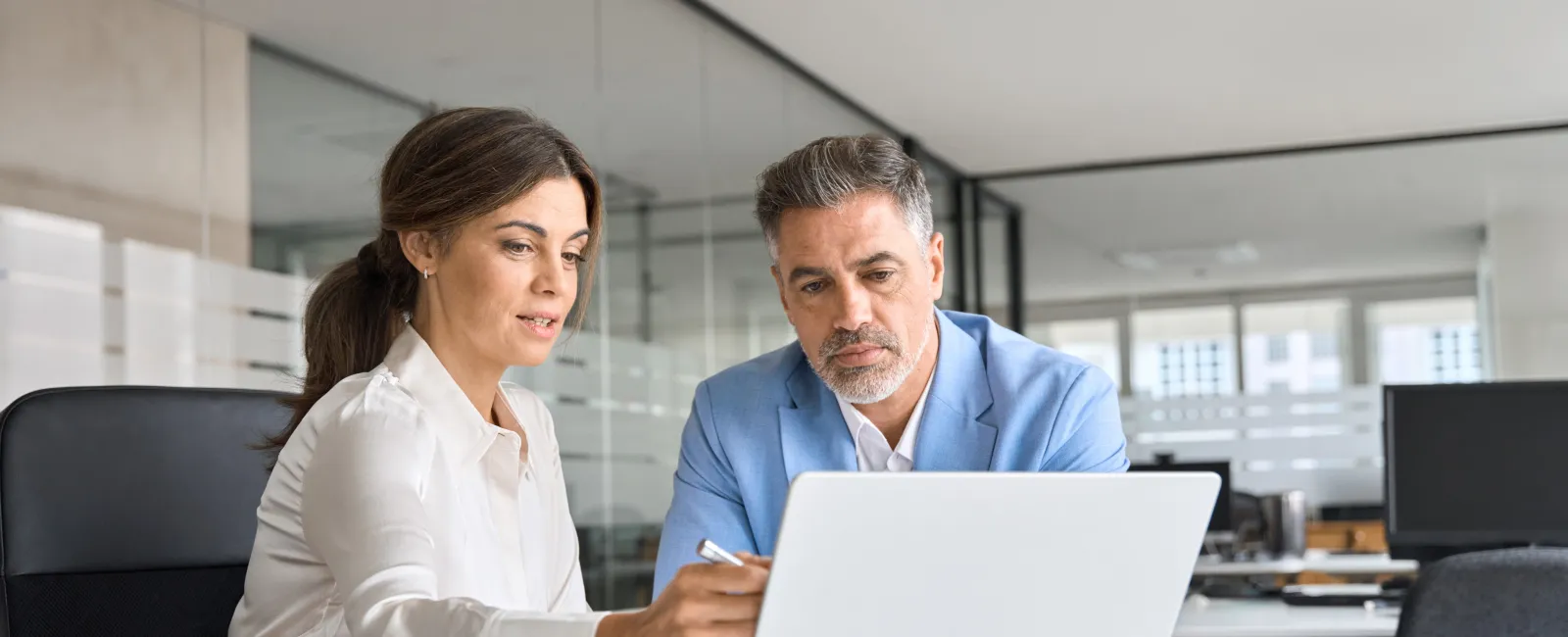 Two business professionals reviewing information together on a laptop in a modern office setting