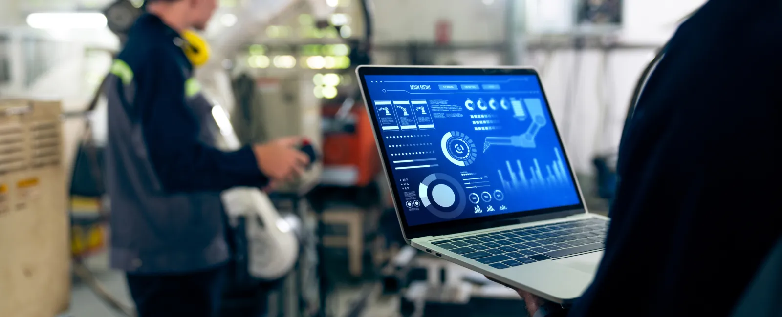 Engineer using laptop with data analytics dashboard in industrial factory environment with worker and machinery