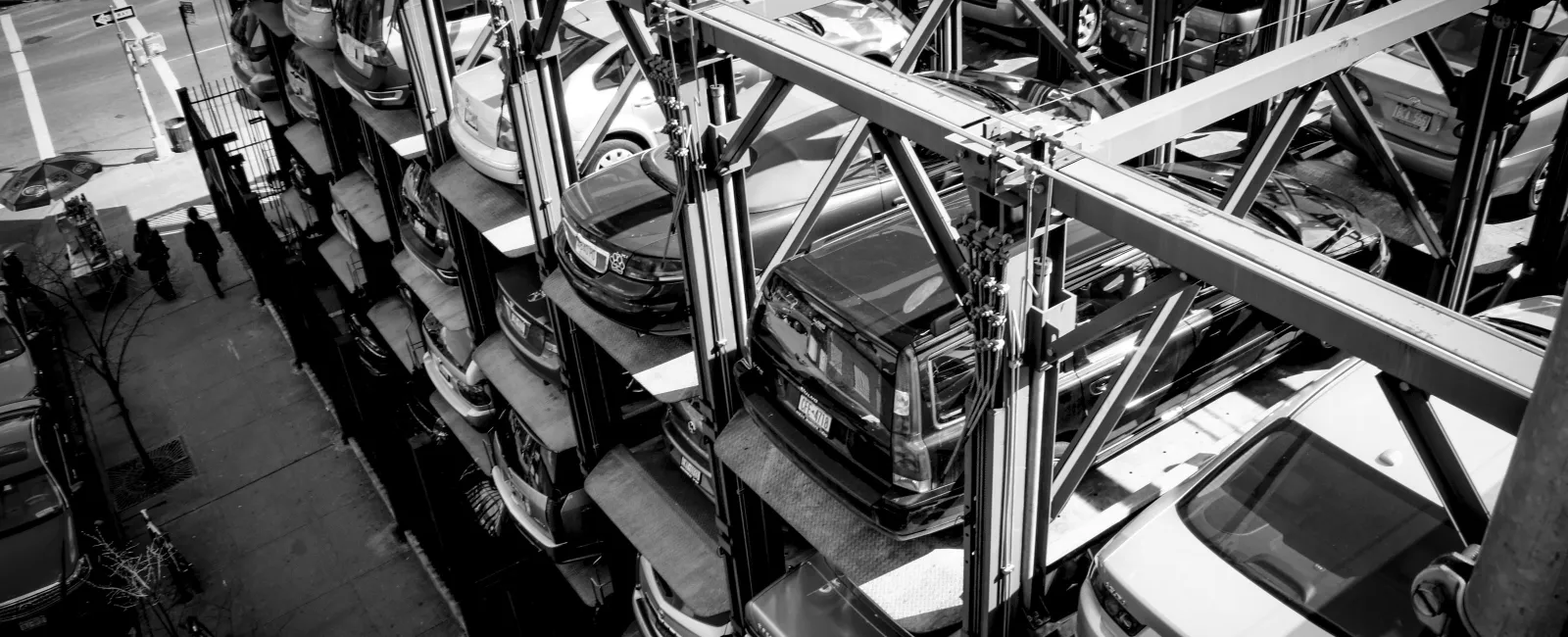 Black and white image of a vertical automated parking structure with multiple cars stacked on platforms.