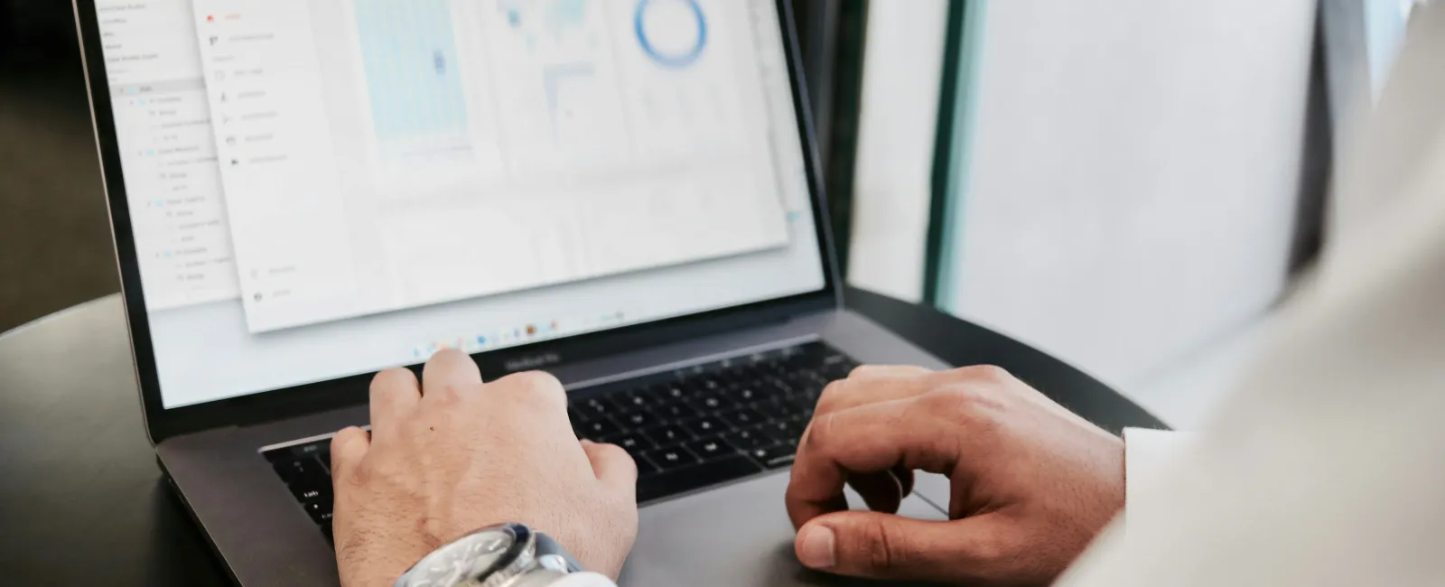 Person analyzing data charts on laptop screen while working at a desk in an office environment.