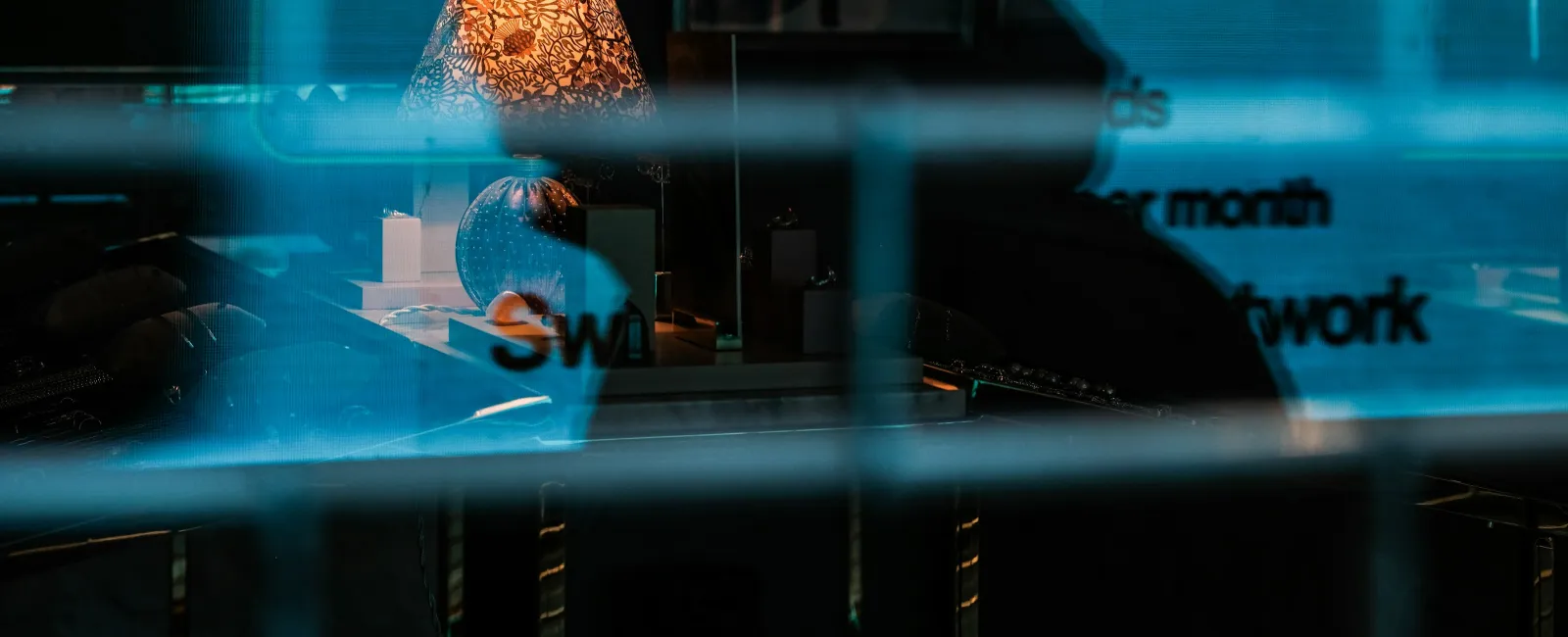 Reflection of a person and a lit floral lamp behind glass with network broadband text in blue tones