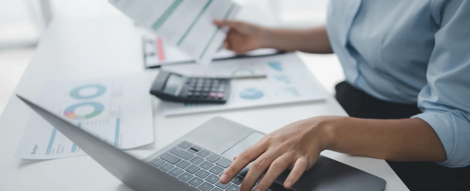 Person working at a desk with laptop, calculator, and financial documents with charts and graphs.