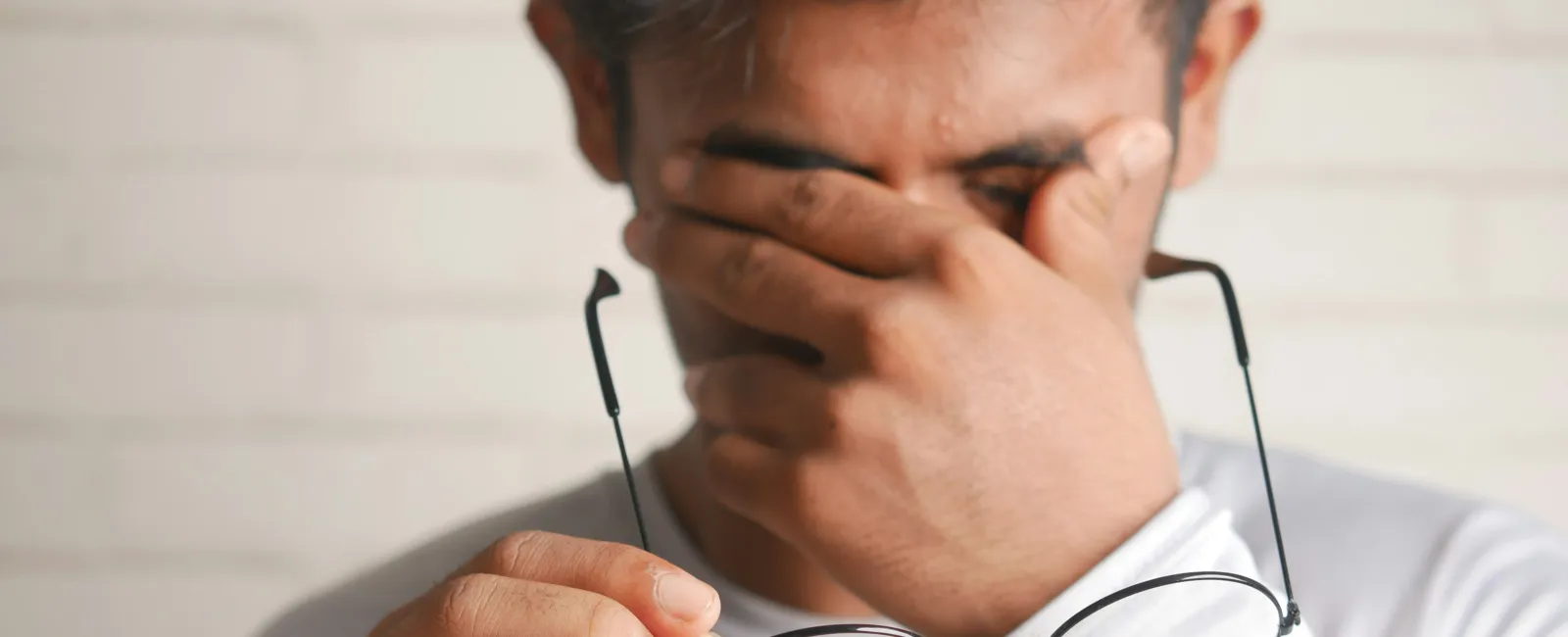 Man removing glasses and rubbing eyes showing eye strain or fatigue wearing white long sleeve shirt.