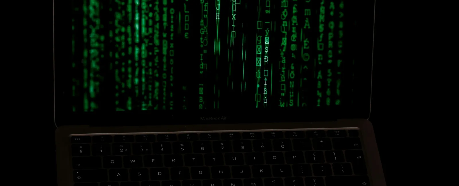 Laptop screen displaying cascading green digital code on black background representing hacking or coding.