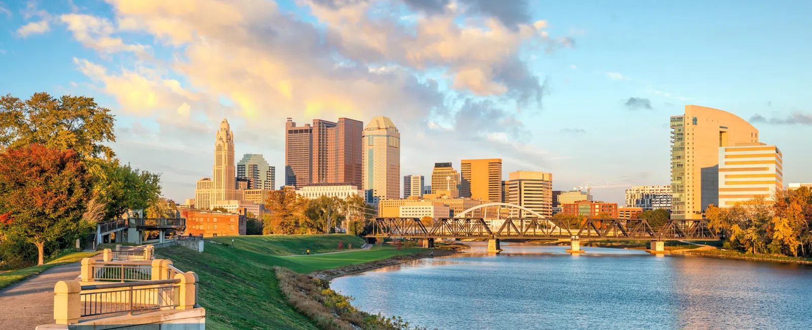 Skyline of Columbus Ohio with river, bridge, autumn trees, and colorful sunset clouds in the sky