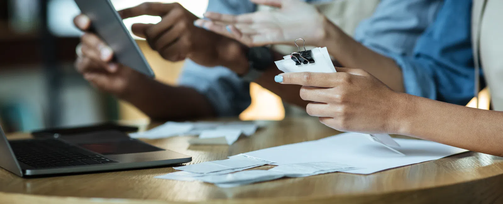 Two people reviewing receipts and using a tablet at a wooden table with a laptop for financial planning.