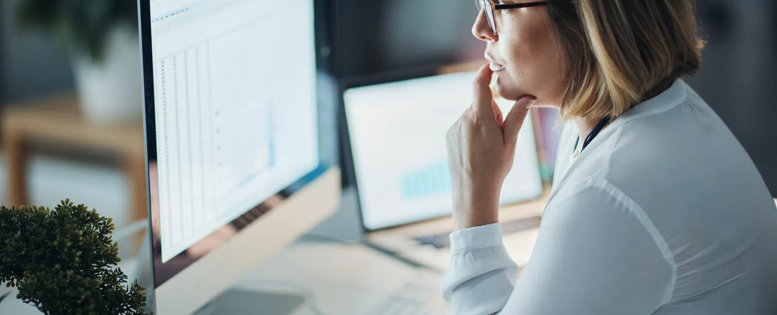Woman analyzing data and charts on desktop computer screen in modern office setting.