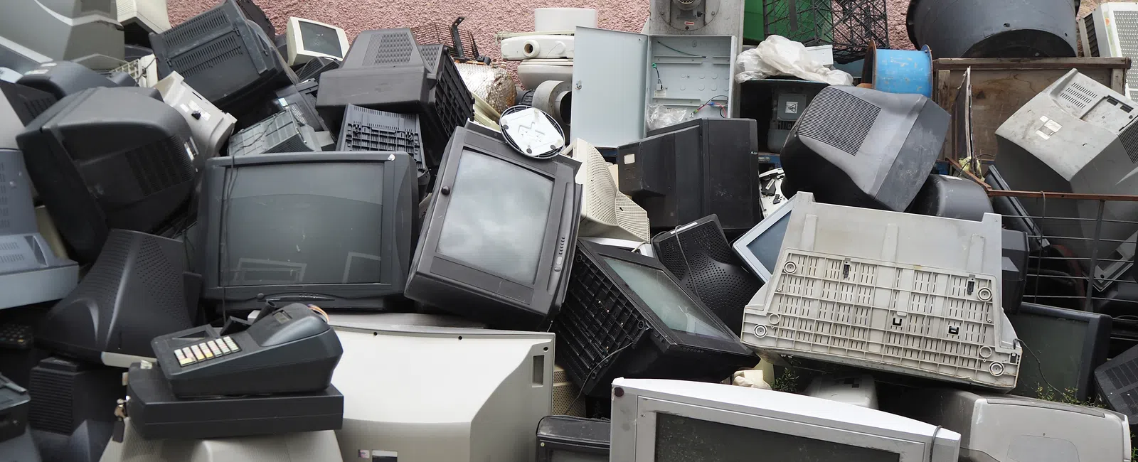 Pile of discarded old CRT televisions and electronics stacked against a pink wall.
