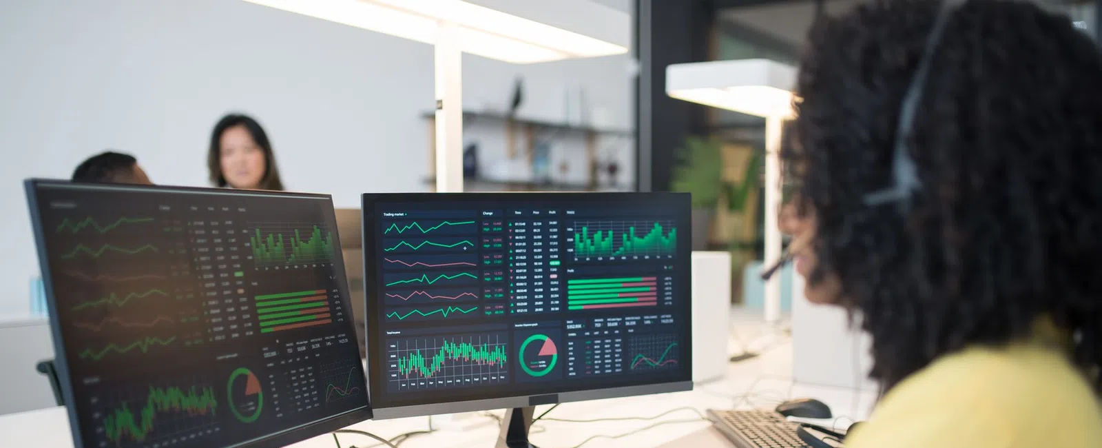 Businesswoman analyzing financial data on dual monitors in a modern office with headset and keyboard