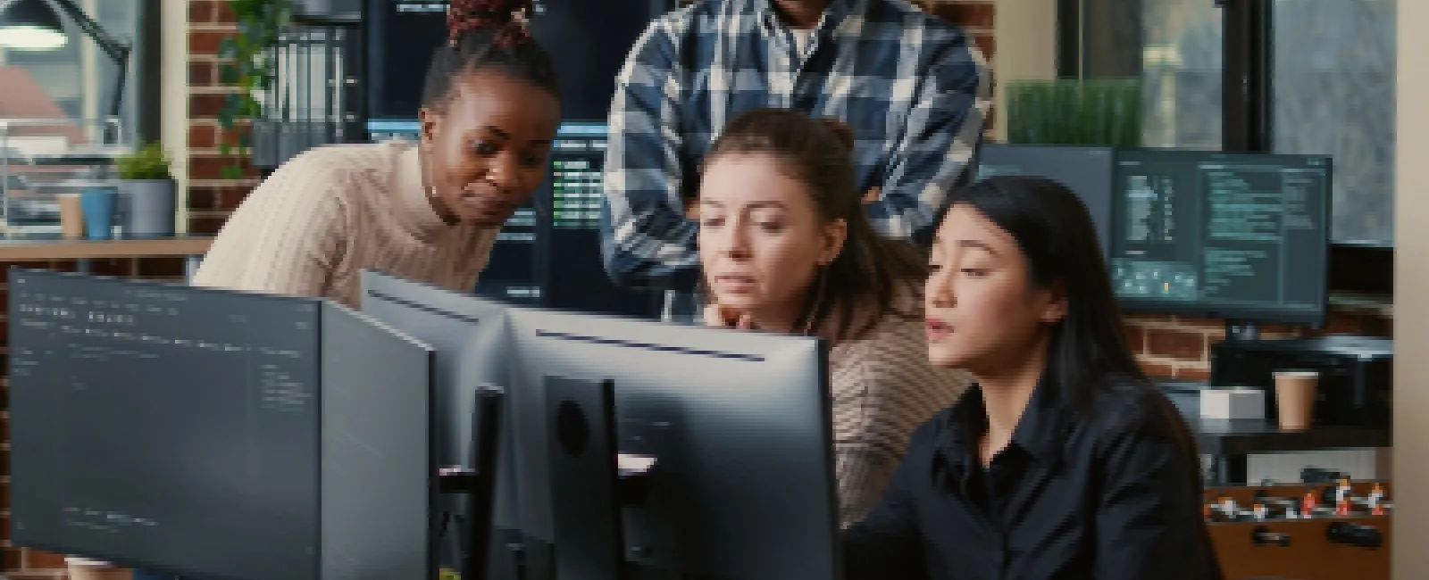 Four diverse tech professionals collaborating and coding together in a modern office with multiple monitors