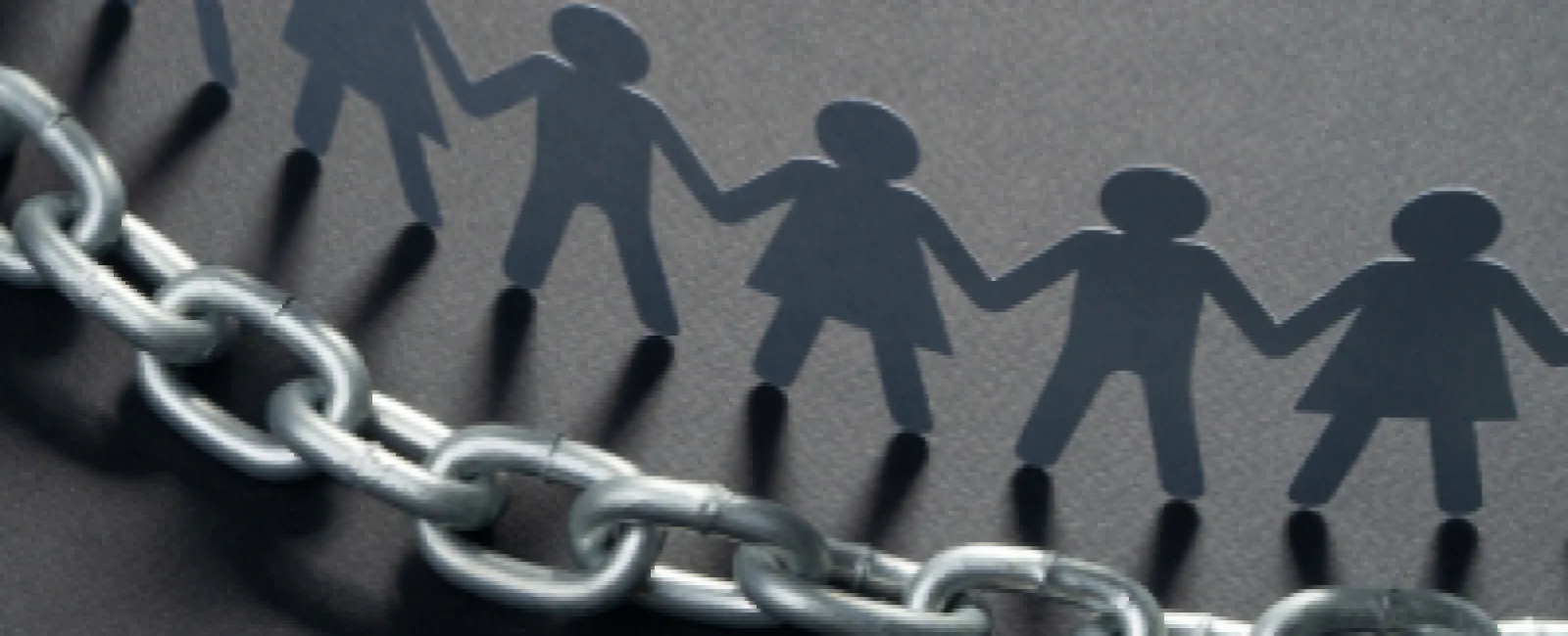 Paper cutout people holding hands forming a chain above a metal chain on dark background representing unity and strength.