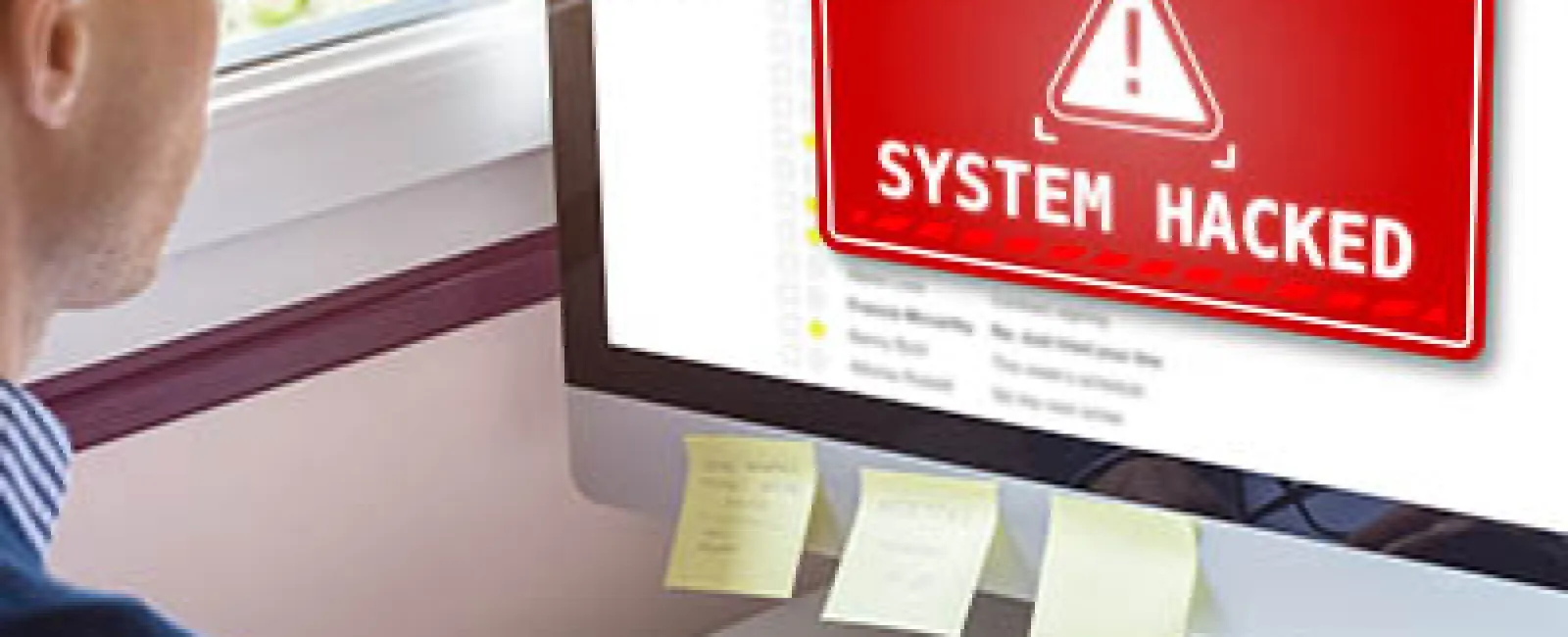 Man working on computer with red system hacked warning displayed on screen in home office.