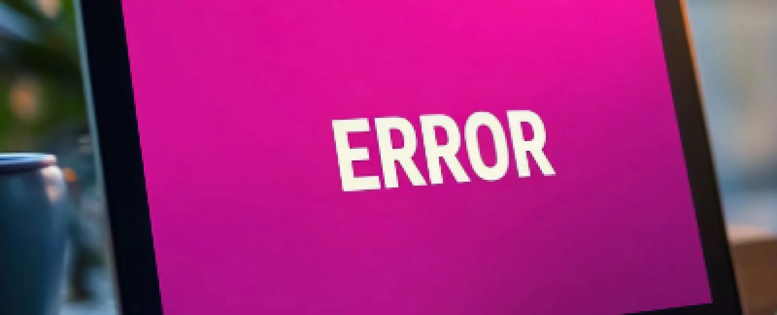 Laptop screen displaying a bold ERROR message on a pink background in a blurred indoor setting.