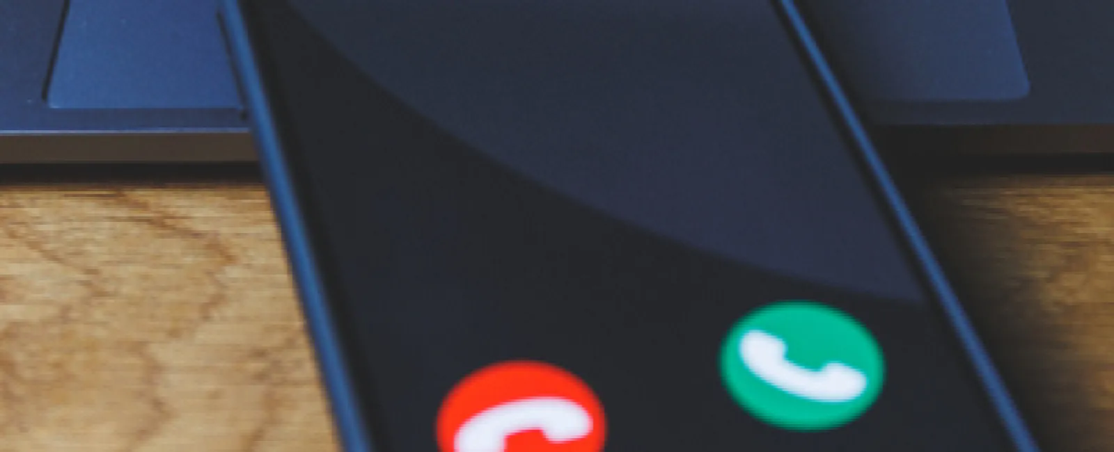 Smartphone on a wooden desk showing an incoming prank call screen with accept and decline buttons.