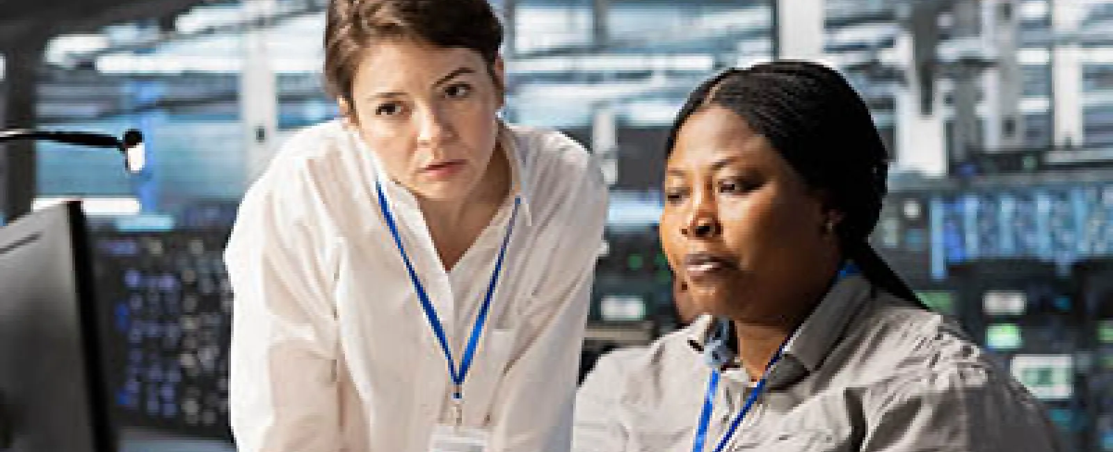 Two female tech professionals collaborating intently at a computer workstation in a modern office.