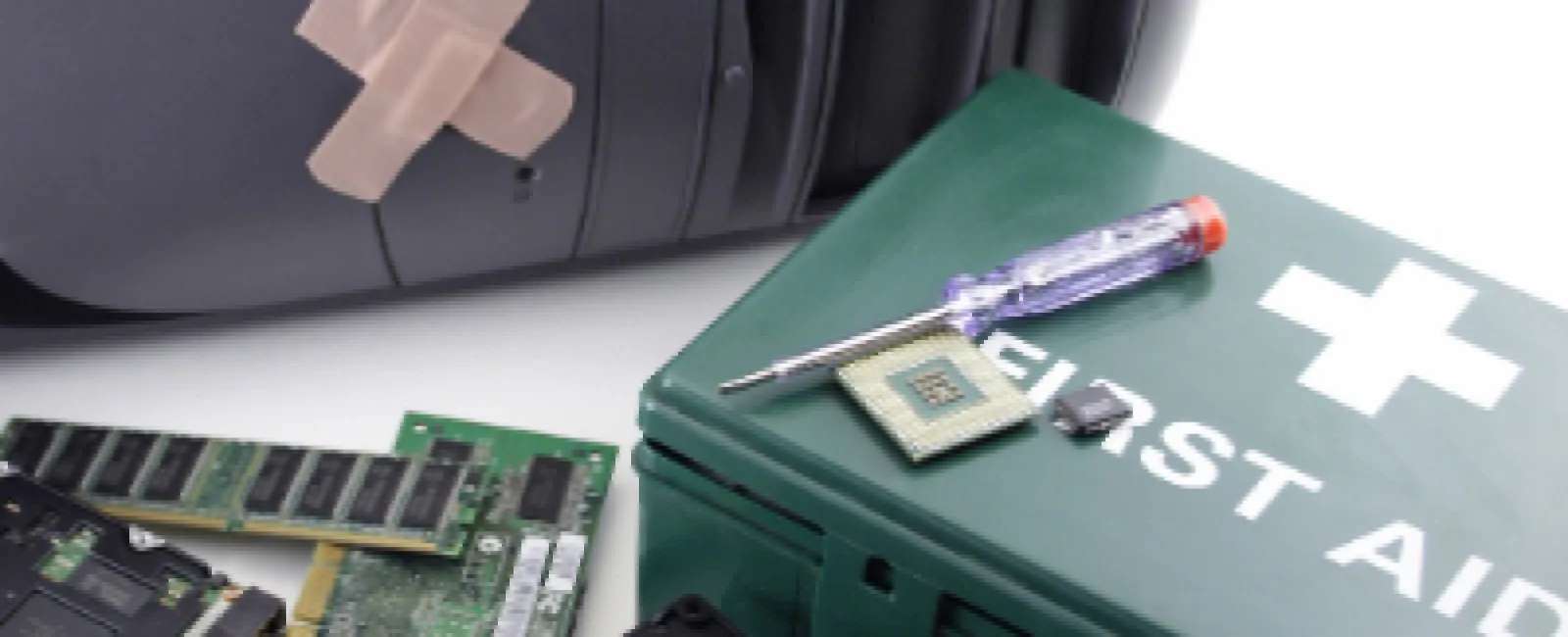 Computer repair kit with a first aid box, screwdriver, CPU chip, computer fan, and motherboard components near a desktop tower.
