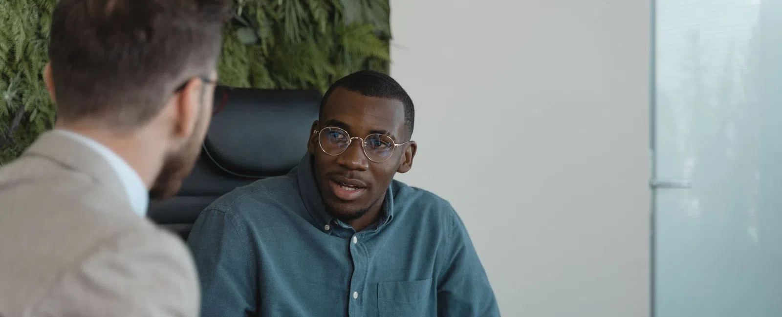 Two men engaged in a professional conversation in a modern office setting with documents and laptop.