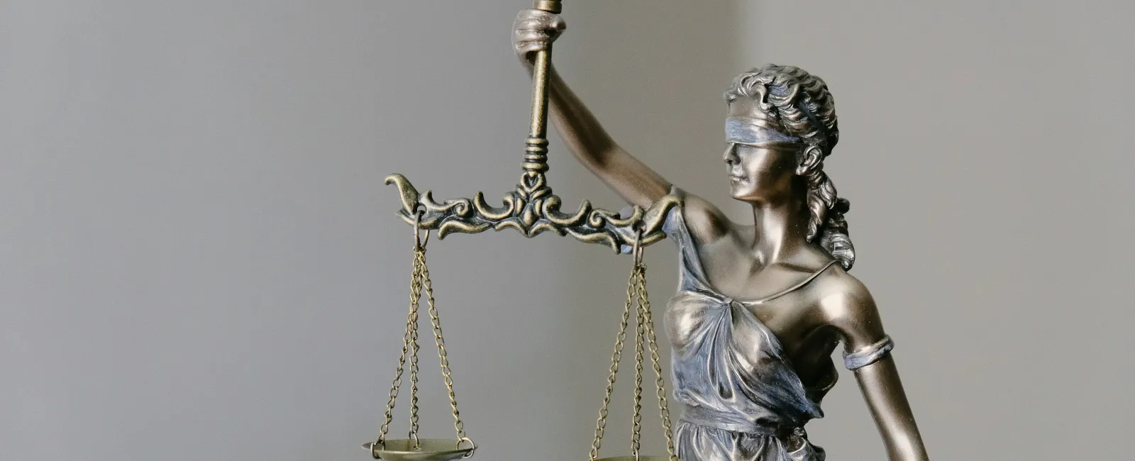 Blindfolded Lady Justice statue holding balanced scales symbolizing fairness and law against gray background
