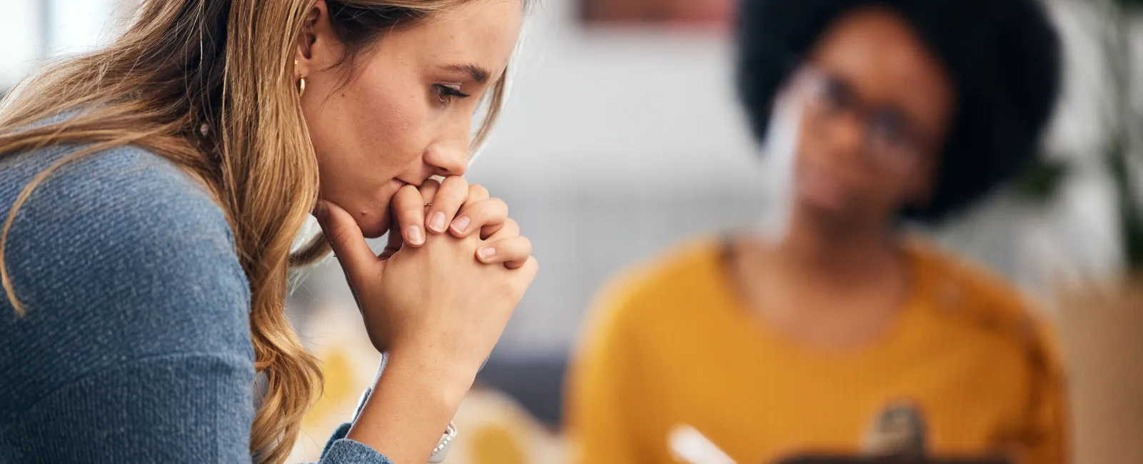 A woman in deep thought during a counseling session with a therapist taking notes in the background.