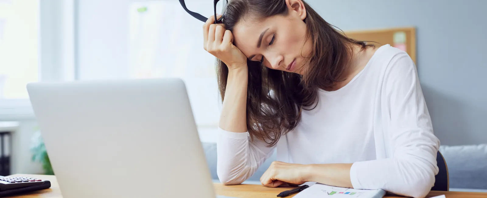 a woman sitting at a desk with a laptop and a pen