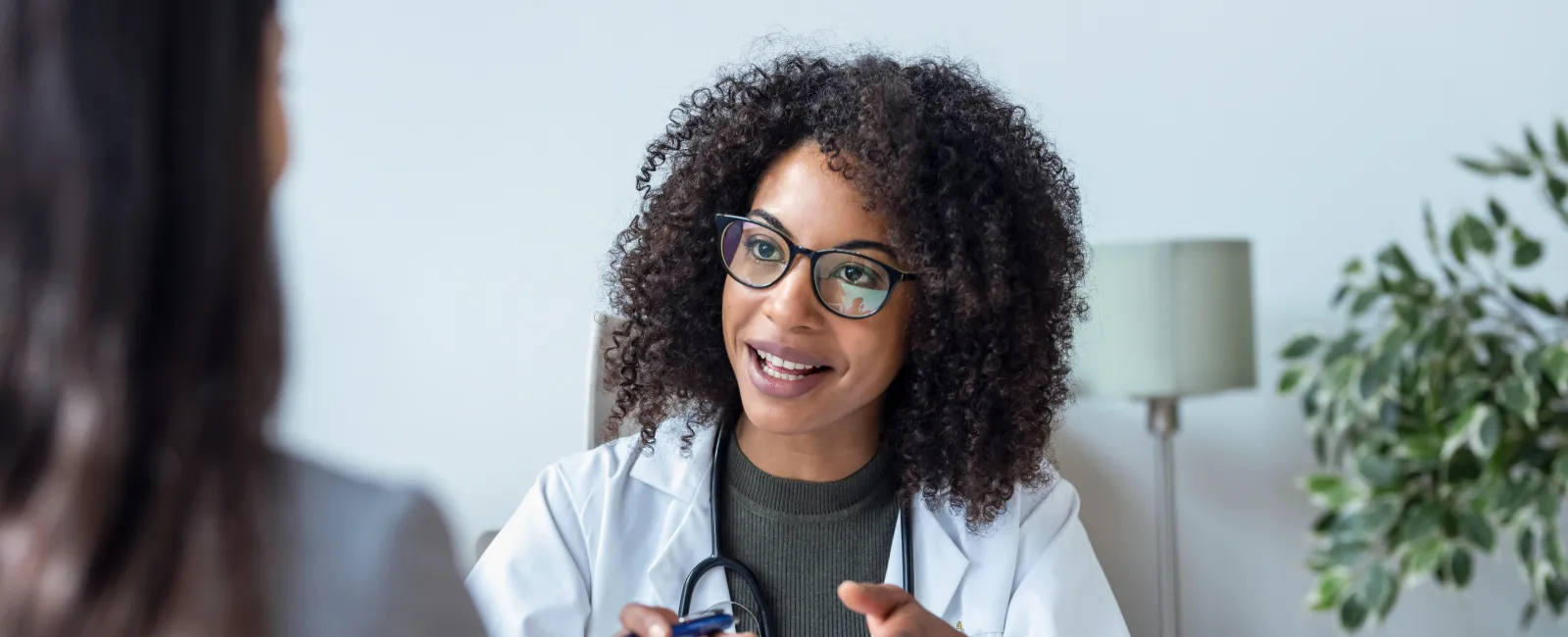 Female doctor in white coat and glasses consulting a patient during an office appointment indoors.