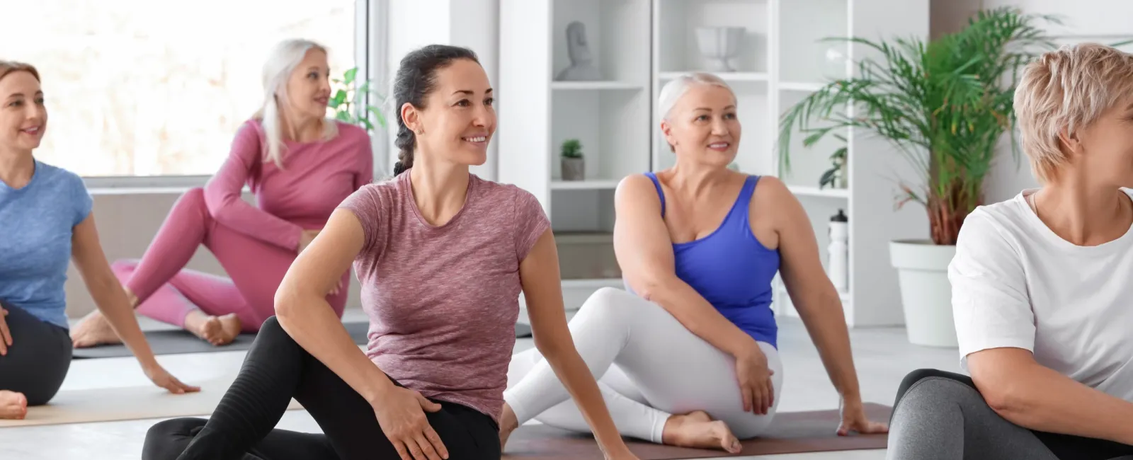 Group of diverse women practicing seated yoga twists in a bright, peaceful studio with yoga mats and plants.
