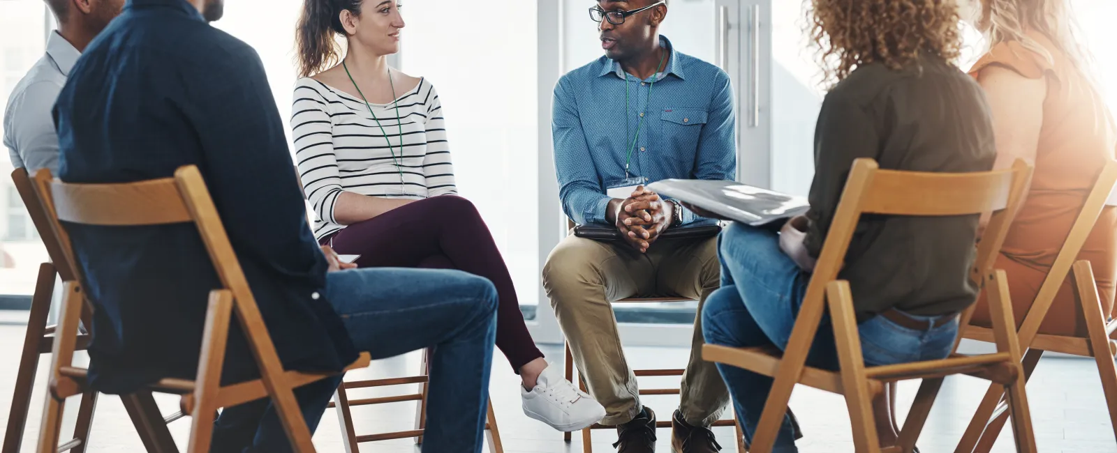 Group of diverse adults sitting in a circle having a discussion in a bright room during a meeting.