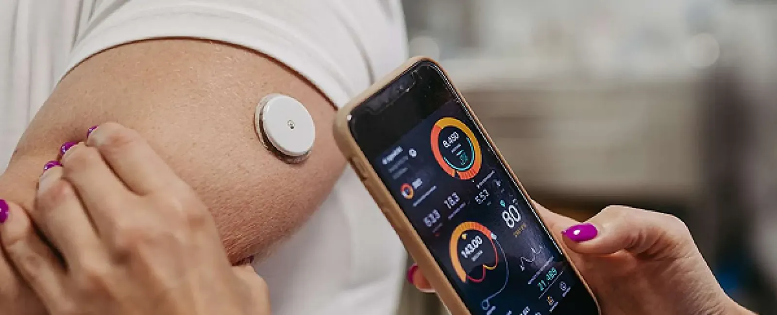 Person wearing a health sensor on their arm with a smartphone displaying health data and vitals.