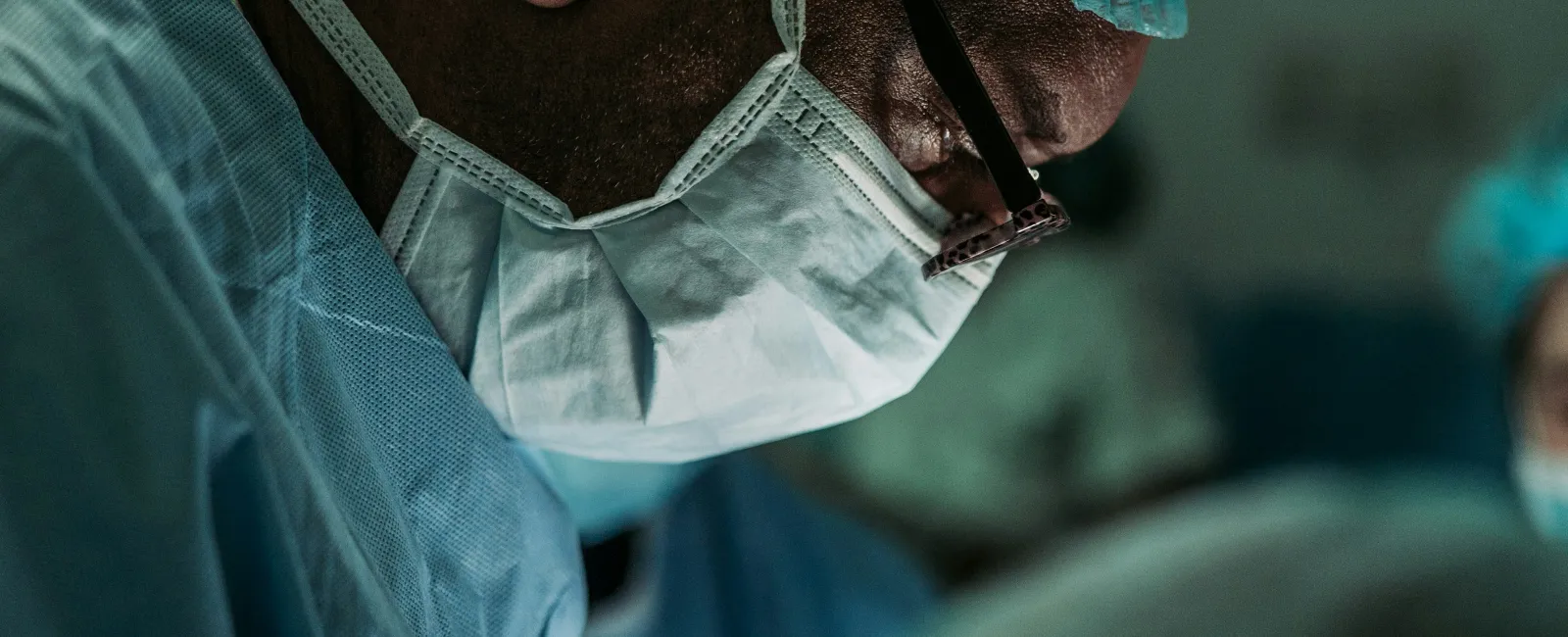 Surgeon wearing protective mask and cap focused on surgery in a sterile operating room environment.