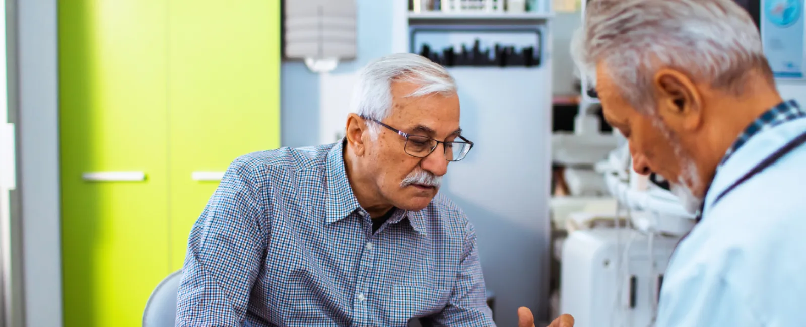 Senior man consulting with doctor in medical office discussing health documents together.