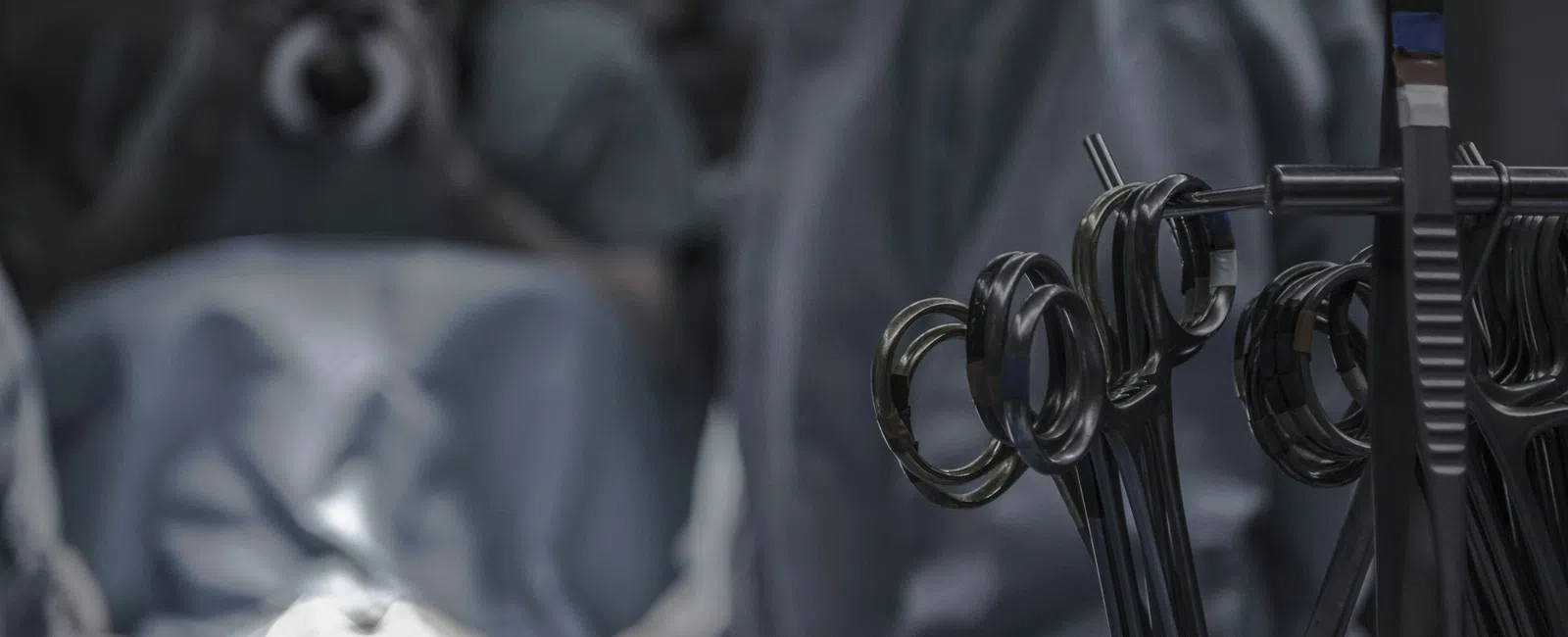 Close-up of surgical instruments with surgeons operating in the background under focused light in an operating room.
