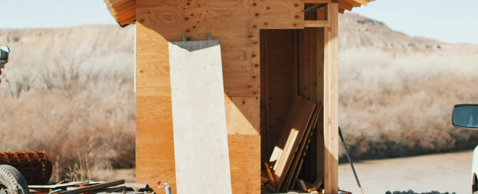 Unfinished wooden shed under construction in a dry, outdoor setting with building materials and tools nearby