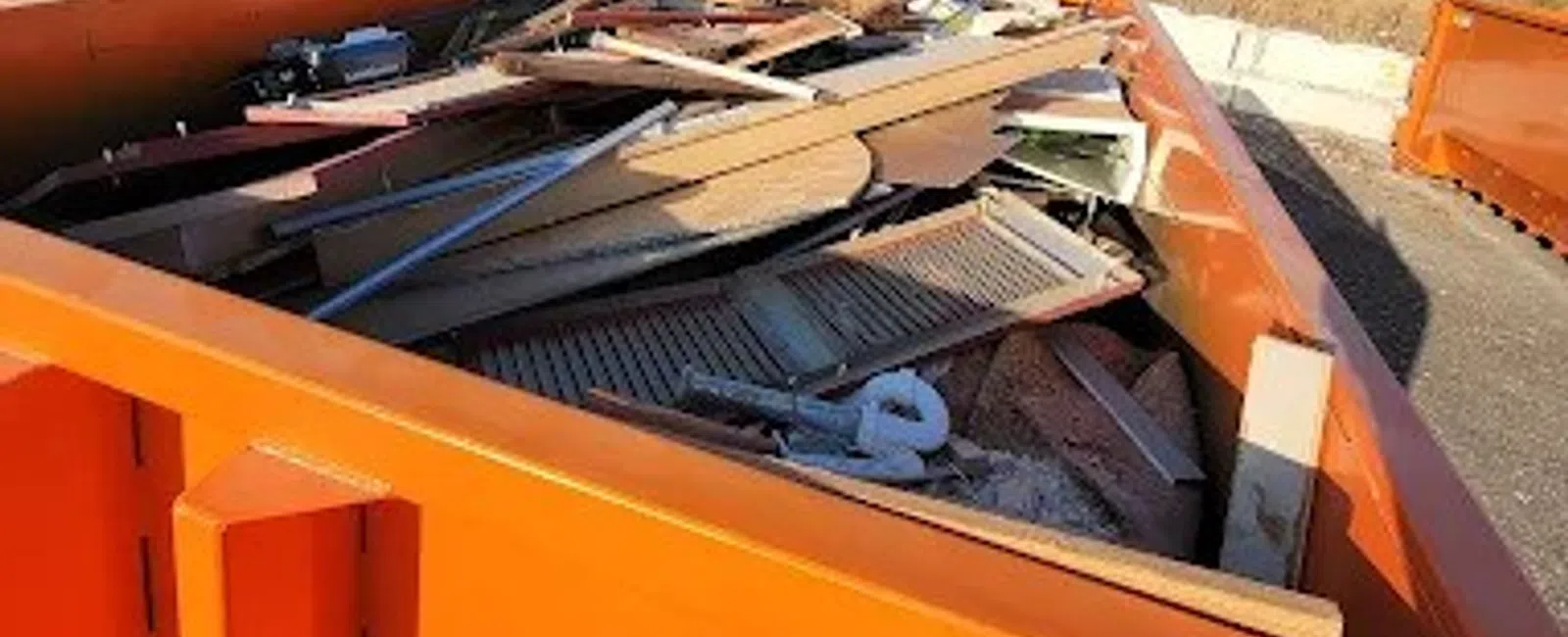 Orange dumpster filled with wood debris and construction waste outdoors on a sunny day.