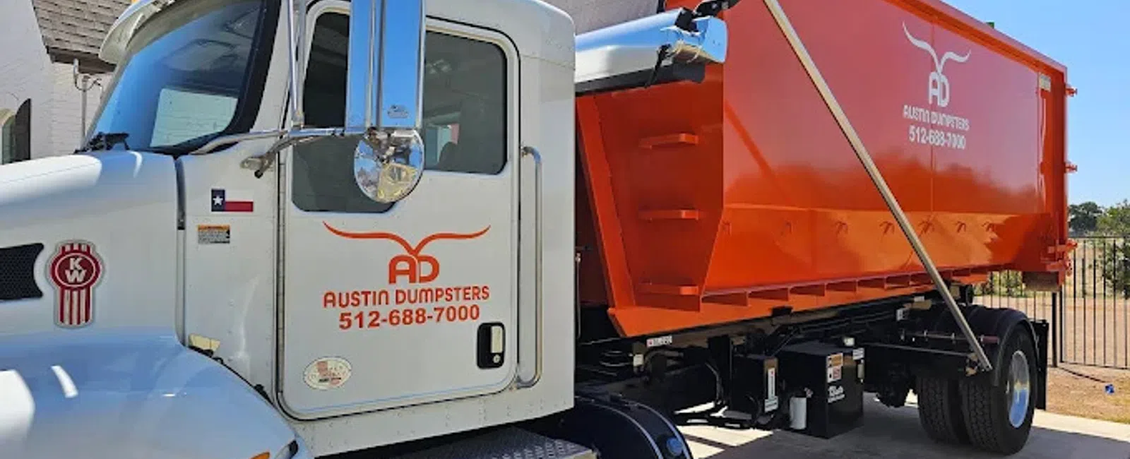 White and orange Austin Dumpsters truck parked outdoors under clear blue sky near a residential area.