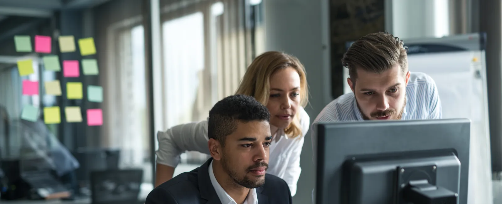Three professionals collaborating and focusing on a computer screen in a modern office environment.