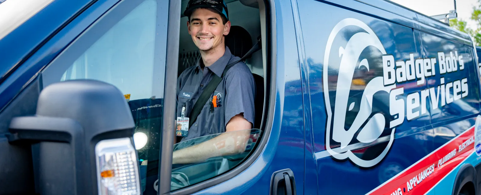 Smiling technician sitting in a blue Badger Bob's Services van with company logo and service details