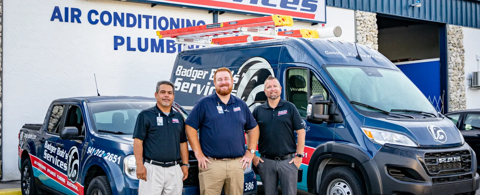 Three Badger Bob's Services workers standing in front of company van and truck outside service building.