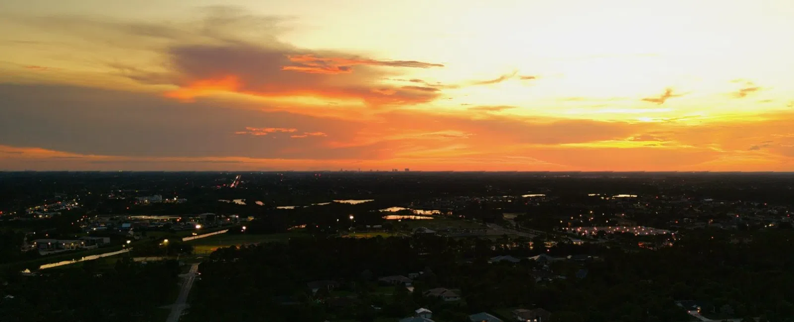 Aerial view of Lehigh Acres at sunset with vibrant orange and yellow sky and scattered clouds representing we offer HVAC near you