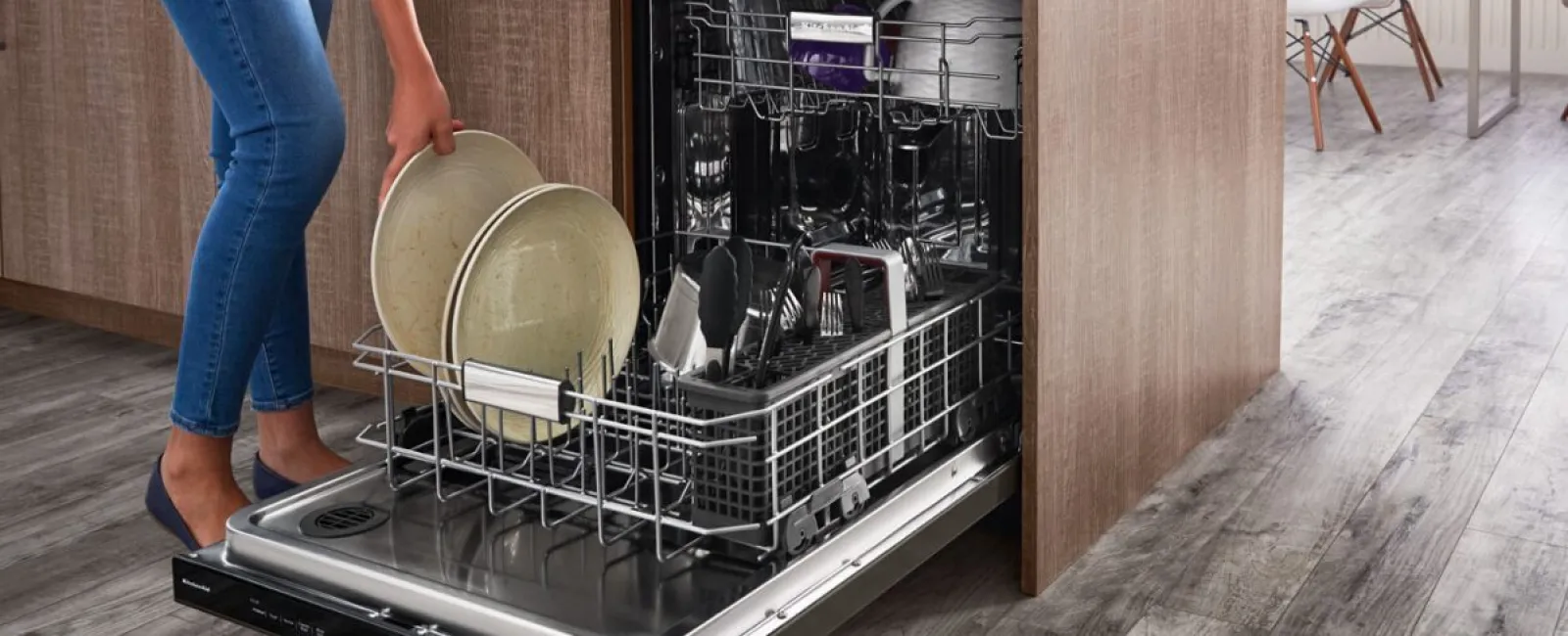 Person loading clean dishes into a modern dishwasher in a cozy kitchen setting.