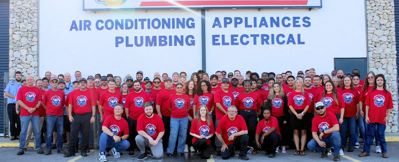 Large group of Badger Bob's Services employees in red shirts outside service center with signage for air conditioning and plumbing.