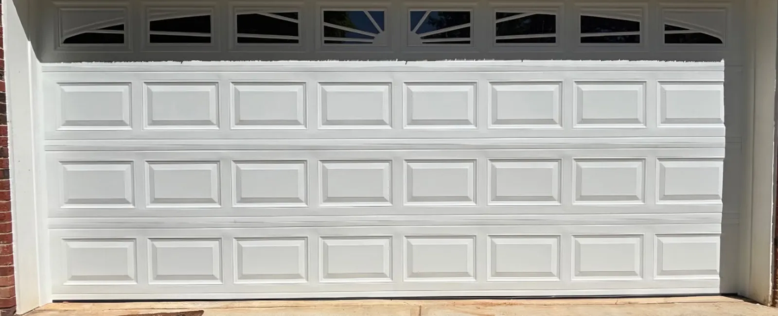 White paneled garage door with small windows above, set in red brick and beige house exterior.