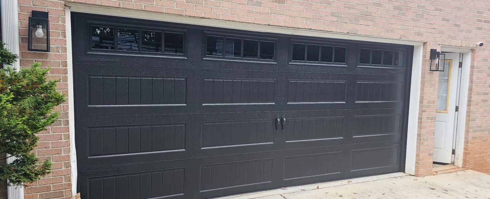 Black sectional garage door with windows on a brick house exterior under daylight.
