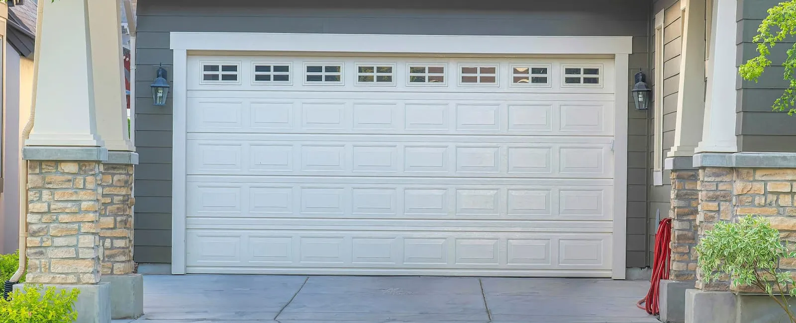 Front view of a modern white garage door with windows, stone pillars, and a concrete driveway.
