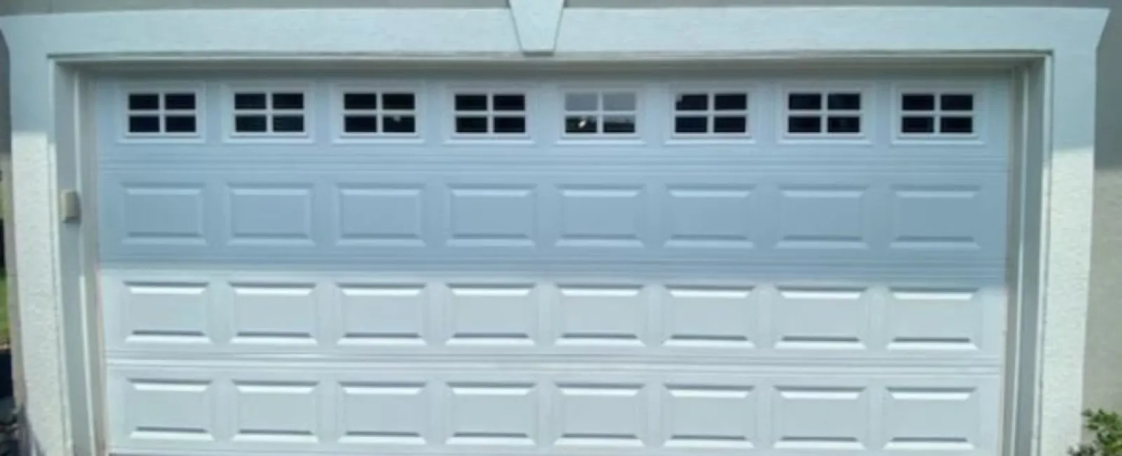 White residential garage door with small upper windows on a driveway under bright daylight.