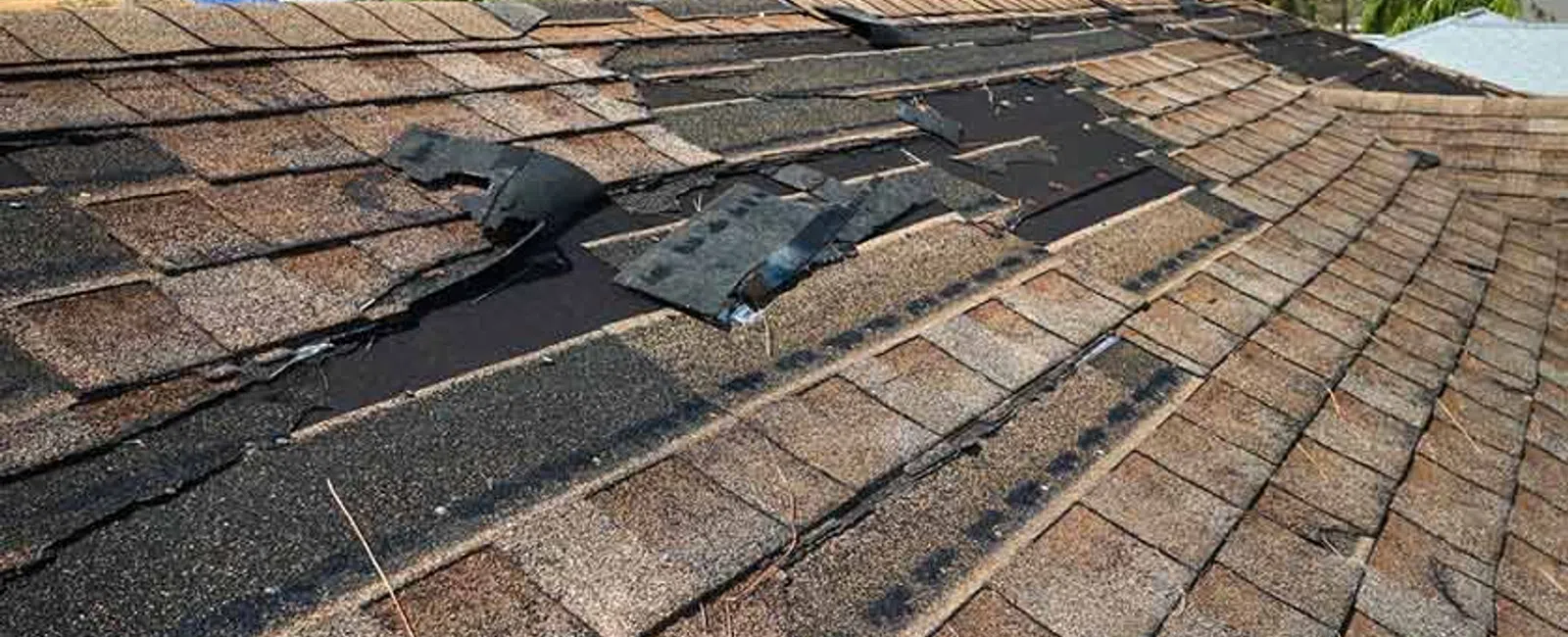 Roof with damaged and missing shingles showing exposed underlayment under a partly cloudy sky.