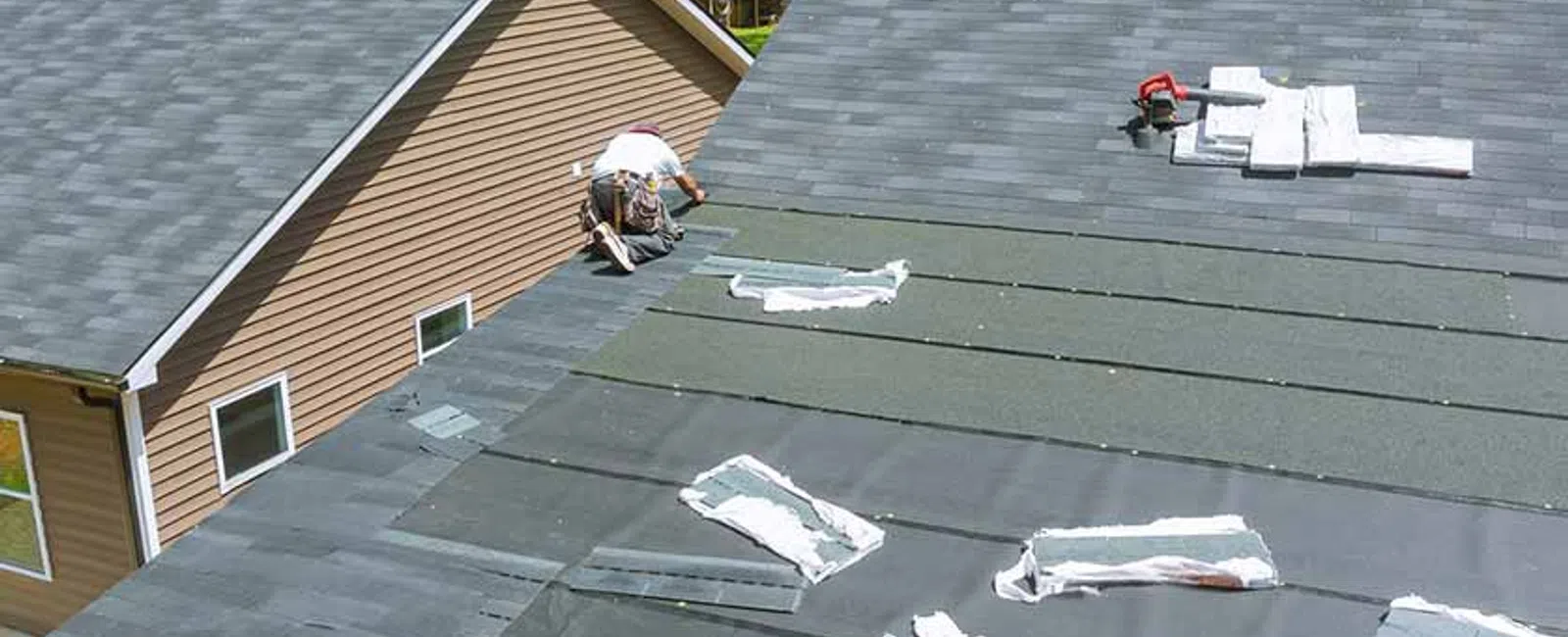 Roofer installing protective underlayment on a residential roof with tools and roofing materials laid out