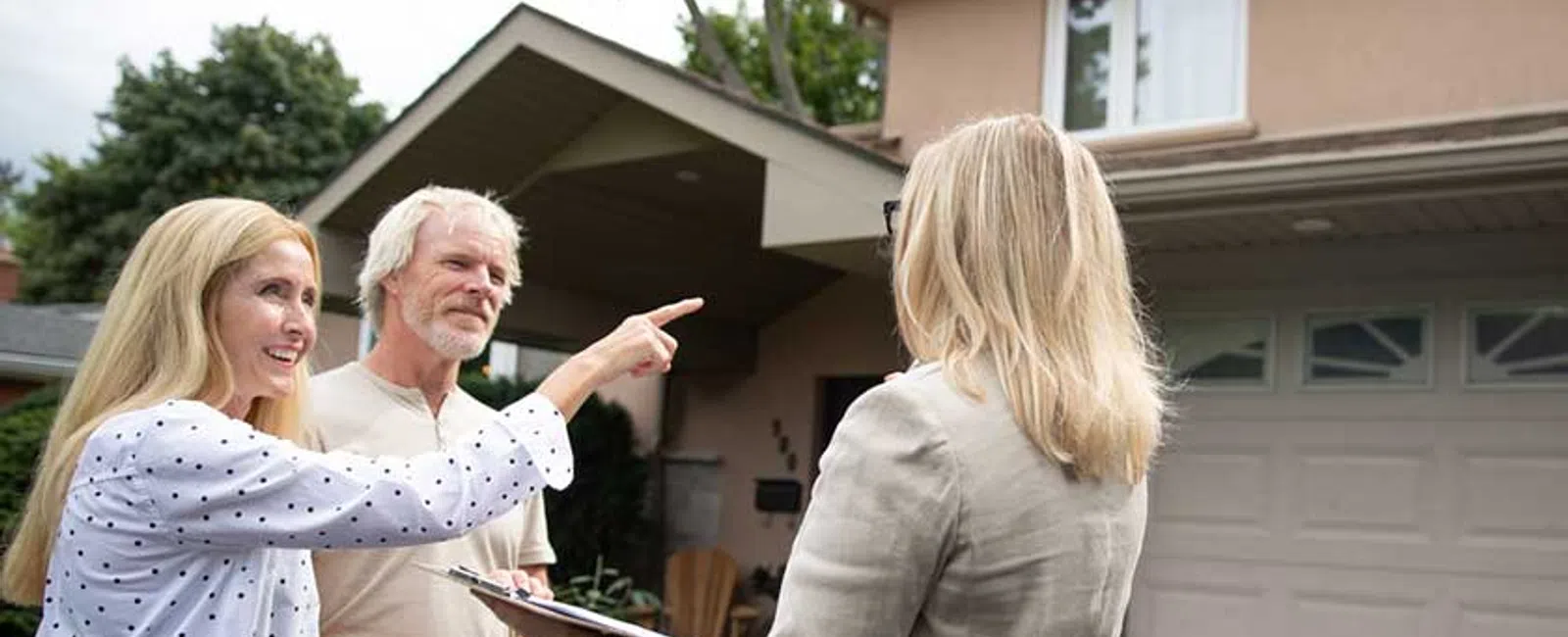 Older couple talking with a real estate agent outside their suburban home near the garage and garden